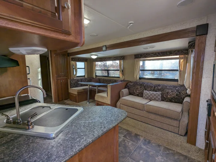 View of a well-equipped RV rental interior, featuring a kitchen counter with sink, a U-shaped dinette, and a comfortable sofa.. Winnebago Sunset Creek 2014