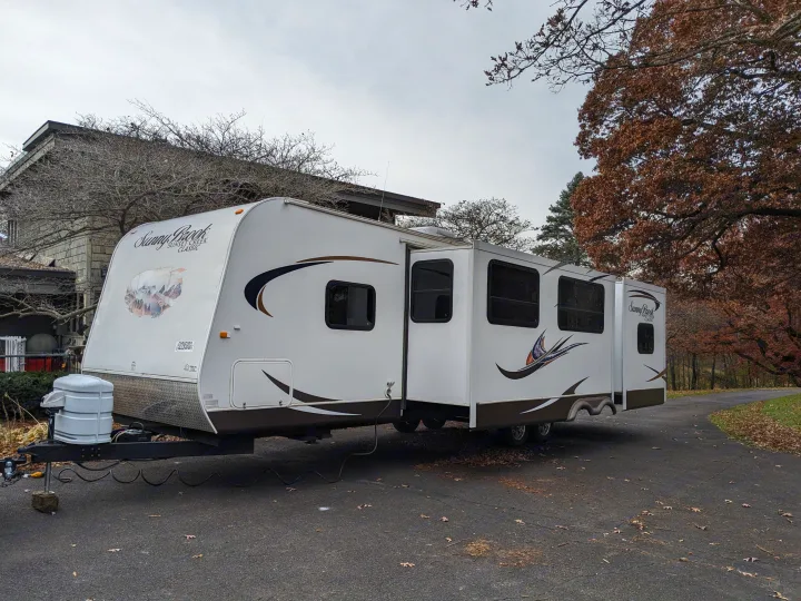 This Sunny Brook travel trailer RV rental, with extended slide-outs, is parked on an asphalt driveway, ready for adventure.. Winnebago Sunset Creek 2014