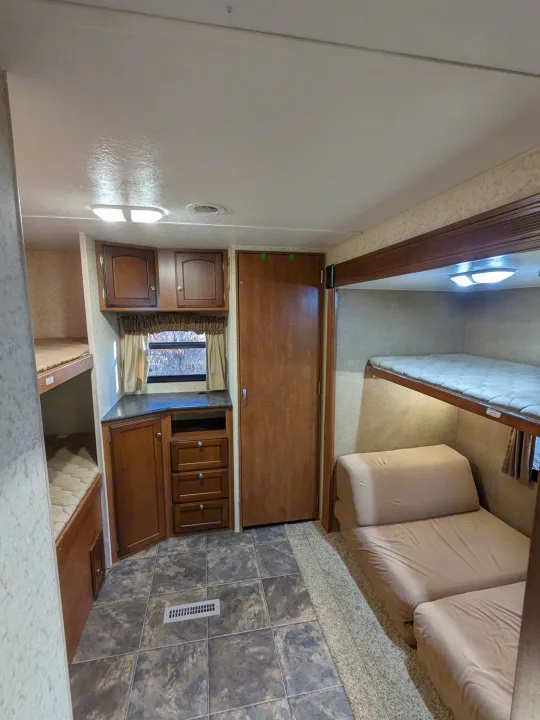 This RV rental interior shows a compact bunkhouse area with three beds, a fold-out sofa, and wood-look cabinetry.. Winnebago Sunset Creek 2014