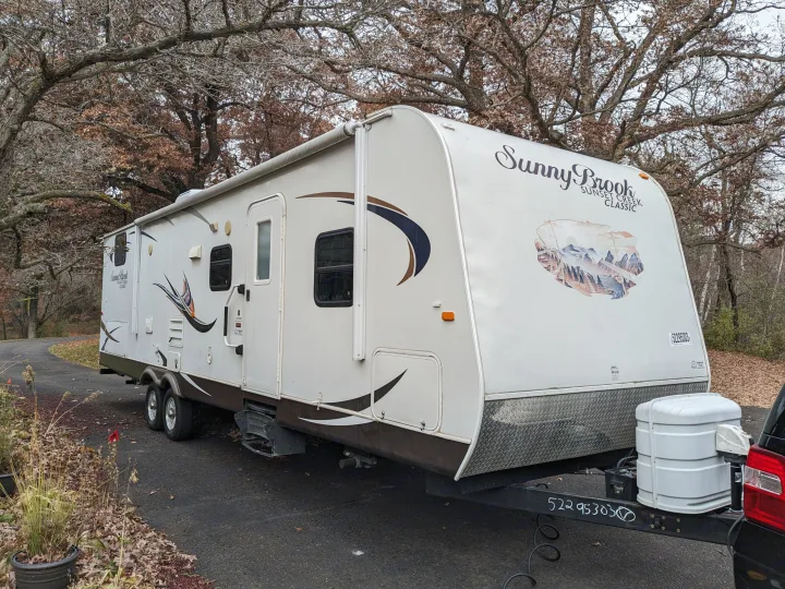 White Sunny Brook travel trailer RV parked on an asphalt drive with autumn trees, ideal for an rv rental.. Winnebago Sunset Creek 2014