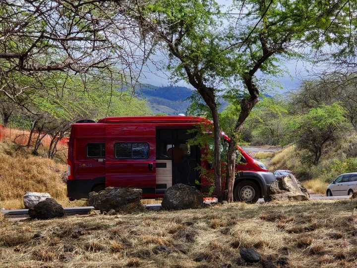 Explore the outdoors! This red Solis RV rental is parked with its door open near trees & mountains.. Winnebago Solis 2022