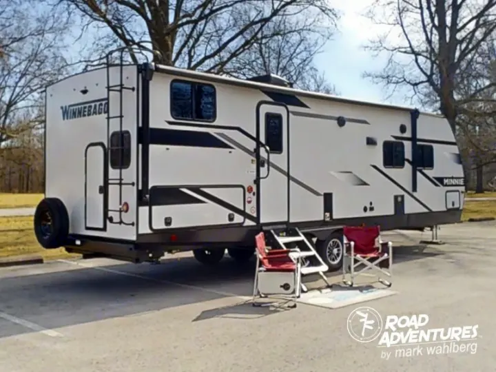 Winnebago Minnie RV rental, parked for a peaceful outdoor getaway. Chairs & rug invite relaxation at this campsite.. Winnebago Minnie 2801BHS 2024
