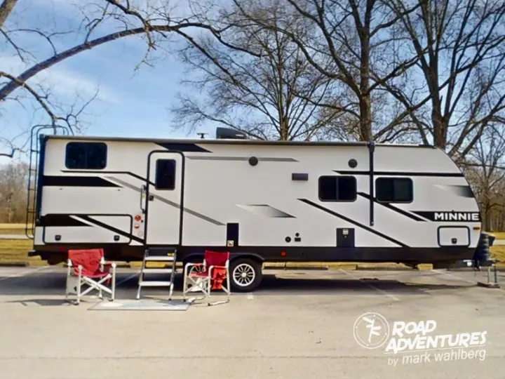This RV rental, a Minnie travel trailer, is set up for outdoor relaxation with chairs at a scenic campsite.. Winnebago Minnie 2801BHS 2024