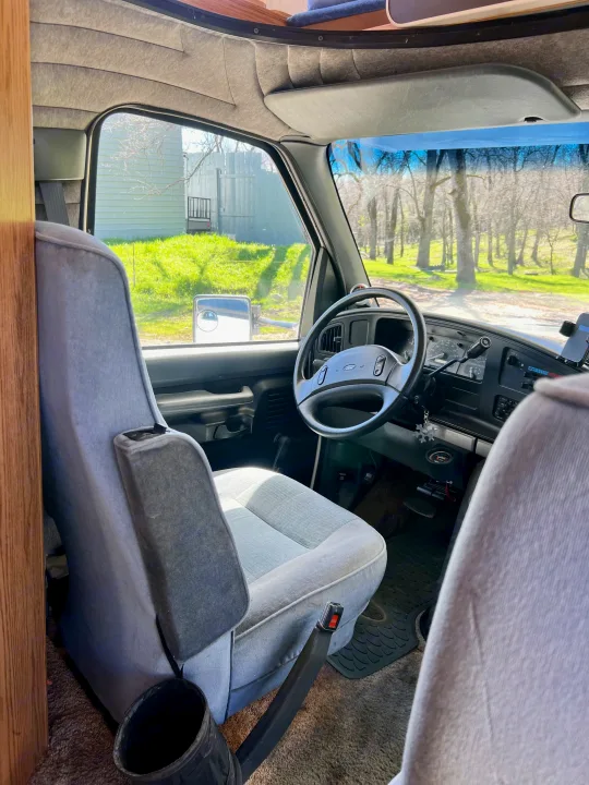 Step inside this RV rental! View of the spacious driver's cabin, featuring gray seats, Ford steering wheel, and dashboard.. Ford Econoline 1994