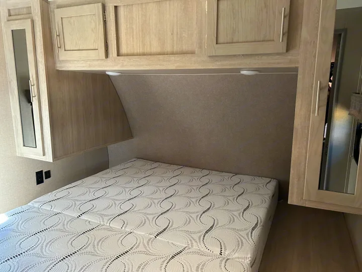 An RV rental's cozy bedroom, featuring a patterned mattress, light wood overhead cabinets, and essential wall outlets.. Coachmen Catalina Legacy 2022