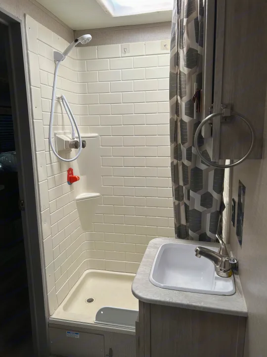RV rental bathroom with a white, molded shower stall, handheld shower, small sink, and gray geometric shower curtain.. Coachmen Catalina Legacy 2022