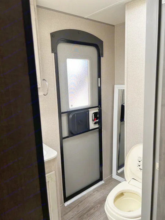 RV rental bathroom interior: A white toilet, small vanity, and an RV screen door are shown.. Coachmen Catalina Legacy 2022
