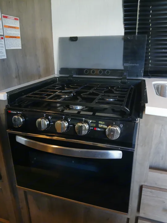 This RV rental features a black Suburban gas stove and oven, perfect for cooking, with visible control knobs and burner grates.. Heartland RVs Pioneer 2022