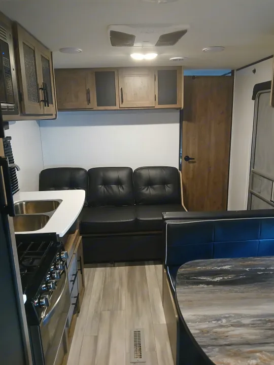 Spacious RV rental interior. Features a compact kitchen with sink/stove, a comfy black sofa, and a dinette booth.. Heartland RVs Pioneer 2022