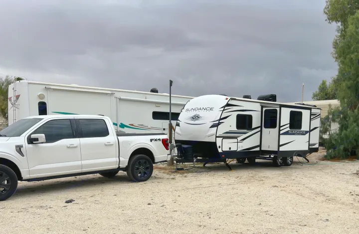 Overcast day at the RV park with a white pickup truck hitched to a Sundance travel trailer RV rental.. Heartland RVs Sundance Ultra Lite 2022