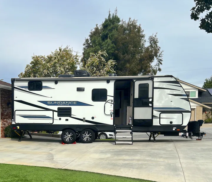 White Sundance Ultra Lite travel trailer, an rv rental, parked on a concrete driveway with its door open.. Heartland RVs Sundance Ultra Lite 2022