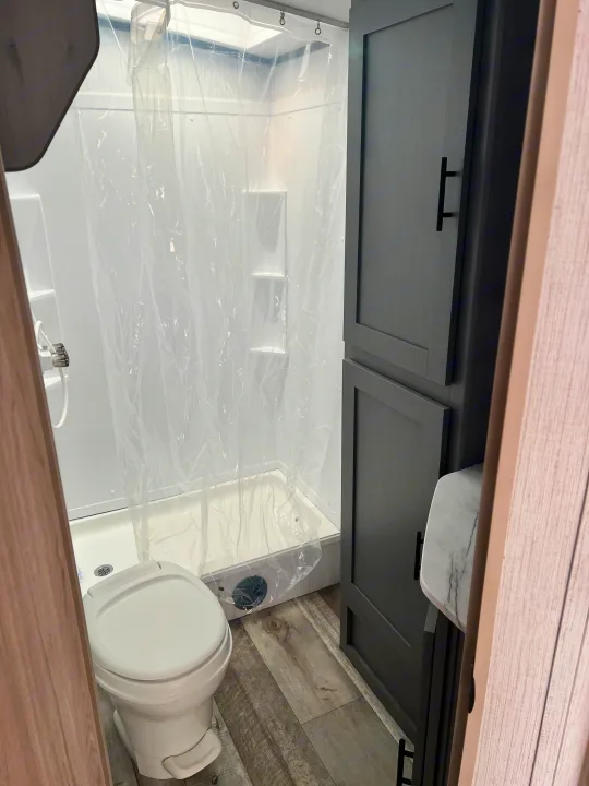 Compact RV rental bathroom: shower with clear curtain, toilet, and dark storage cabinets. Ideal for your travel trailer adventures.. Heartland RVs Sundance Ultra Lite 2022