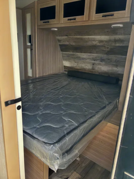 Spacious RV rental bedroom with a new grey mattress, sleek wood-grain walls, and convenient overhead storage cabinets.. Heartland RVs Sundance Ultra Lite 2022