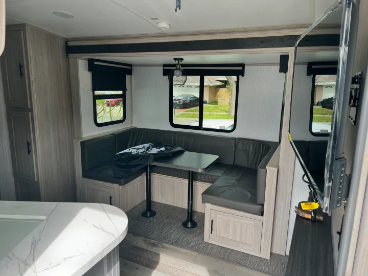 View inside an rv rental, showing a U-shaped dinette with dark seating & table, light wood cabinetry, and a TV.. Heartland RVs Sundance Ultra Lite 2022