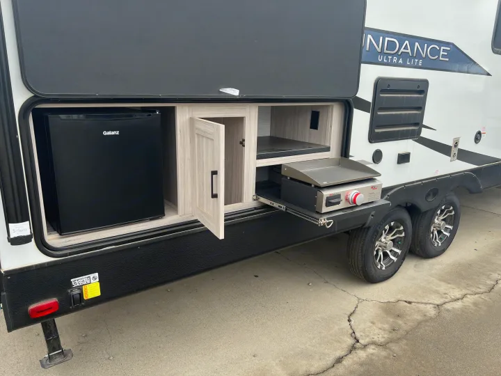 This RV rental's outdoor kitchen setup includes a Galanz mini-fridge and pull-out griddle, ideal for convenient camping.. Heartland RVs Sundance Ultra Lite 2022