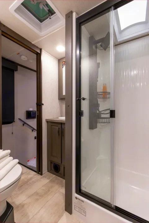 Modern RV rental bathroom: glass shower, toilet, vanity, and light wood-look flooring. Clean and functional design.. Grand Design Momentum M-Class Toy Hauler 2023