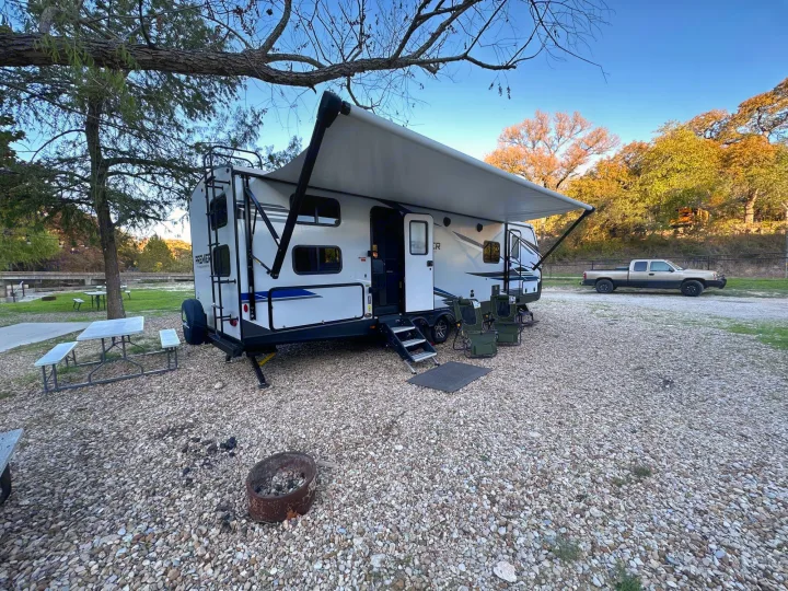 Experience camping with this RV rental: A white travel trailer, awning extended, chairs, and fire pit on a gravel site.. Keystone RV Bullet Premier Ultra Lite 2022