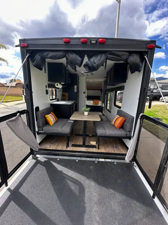 Inside a modern **rv rental**: open rear ramp forms a patio, revealing dining, kitchen, and sleeping areas.. Forest River Cherokee Wolf Pup 2021