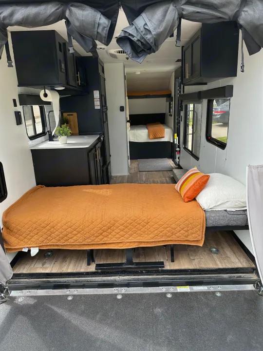 Inside a modern RV rental: kitchen, sofa bed, and bunk area with wood floors, viewed from the open rear ramp.. Forest River Cherokee Wolf Pup 2021