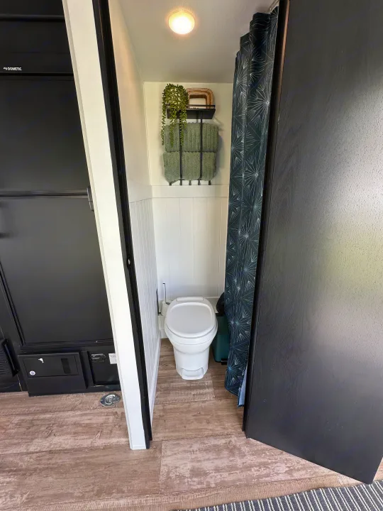 Compact and clean RV rental bathroom featuring a white toilet, patterned shower curtain, and organized storage.. Forest River Cherokee Wolf Pup 2021
