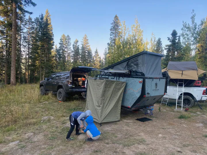 Campsite in a forest with an SUV, teardrop trailer, and truck with rooftop tent. Great for an RV rental adventure as kids play.. Mission Overland Mission Overland Trailer 2020