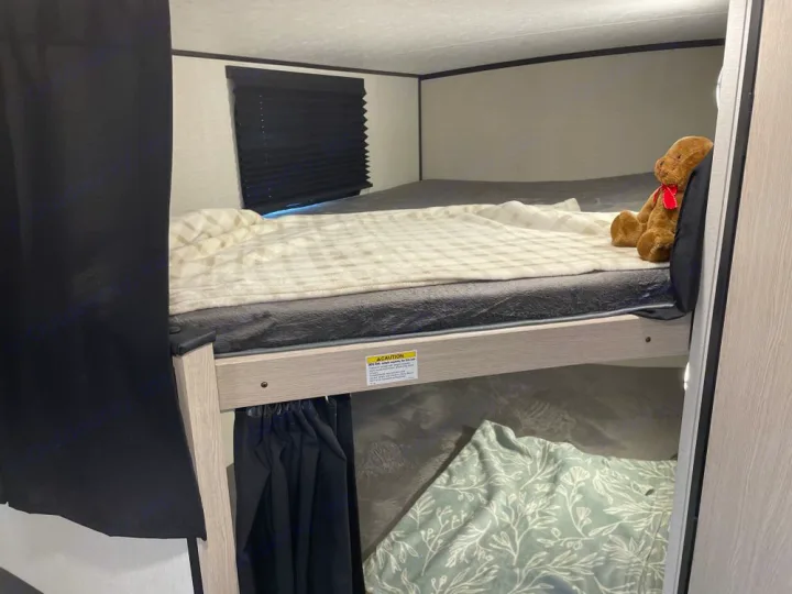Cozy bunk beds in an RV rental. Top bunk with a teddy bear, bottom with a green blanket, both have privacy curtains.. Coachmen Apex Nano AAPT186BH 2024