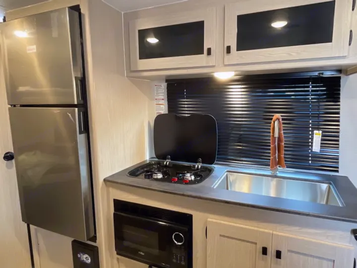Compact RV rental kitchen: stainless steel fridge, sink, two-burner stove with cover, and a microwave.. Coachmen Apex Nano AAPT186BH 2024
