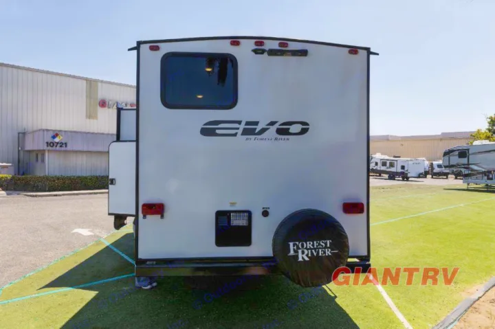 Rear view of a white Forest River Evo travel trailer, ideal for rv rental. Parked on artificial grass with a building behind.. Forest River Evo CSJT2650G 2023