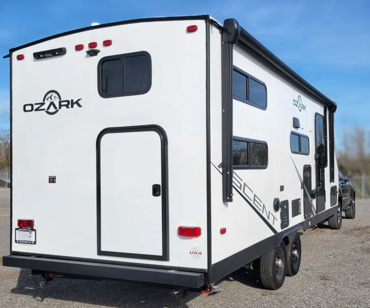 White Ozark travel trailer for rv rental, seen from the rear and side, showing windows, doors, and a retracted awning.. Forest River ozark 2440bhkx 2024