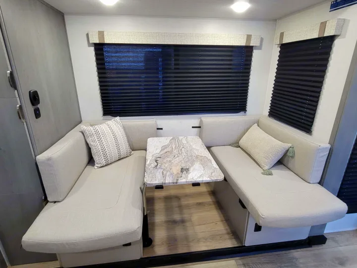Modern RV rental dinette area featuring U-shaped light gray seating, a marble-look table, and dark pleated blinds.. Forest River ozark 2440bhkx 2024