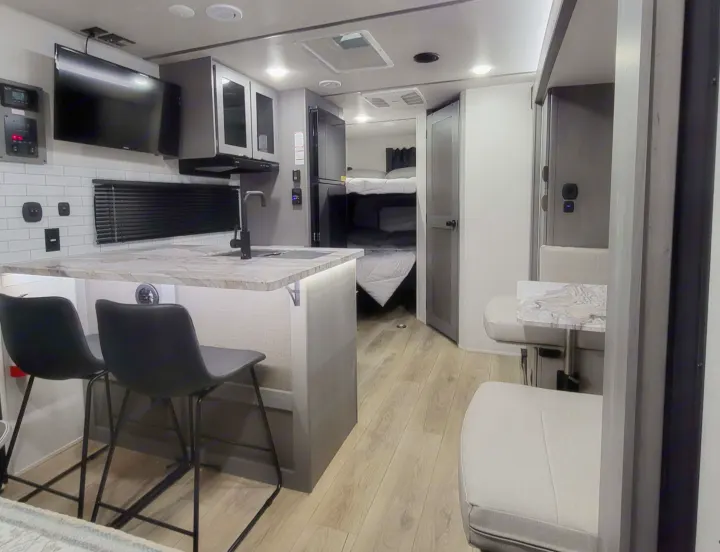 Modern RV rental interior with a kitchen island, stools, dining booth, bunk beds, TV, and full kitchen amenities.. Forest River ozark 2440bhkx 2024