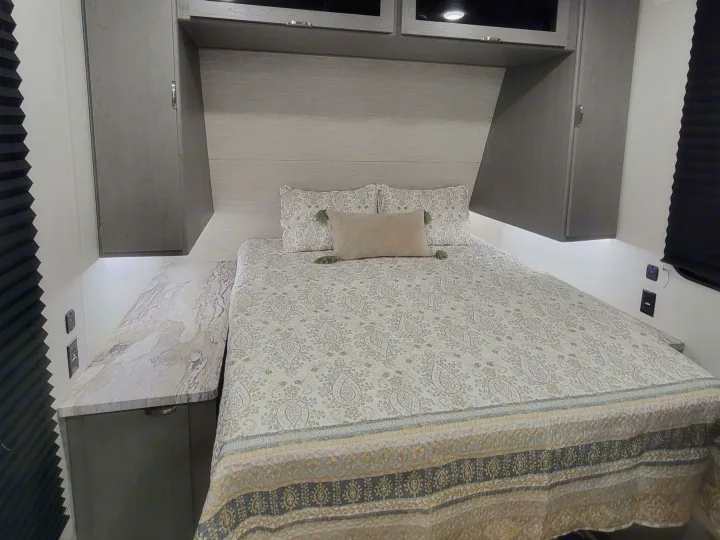 Comfortable RV rental bedroom featuring a patterned bed, modern overhead cabinets, and convenient bedside tables with outlets.. Forest River ozark 2440bhkx 2024