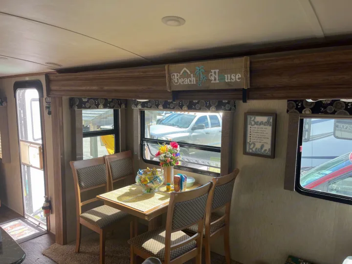 Inside an RV rental, a well-lit dining area features a table, chairs, beach decor, and scenic window views.. Keystone Laredo 2015