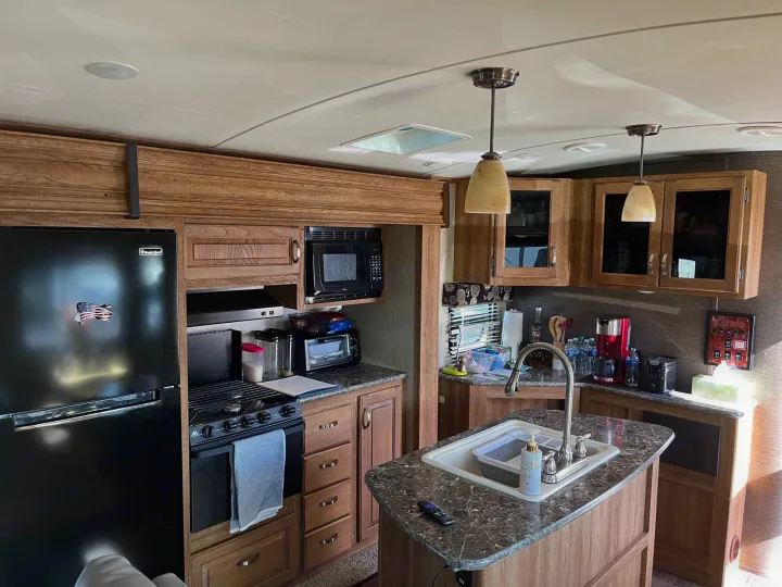 Fully equipped RV rental kitchen: black fridge, stove, microwave, and island sink. Ready for your next adventure.. Keystone Laredo 2015