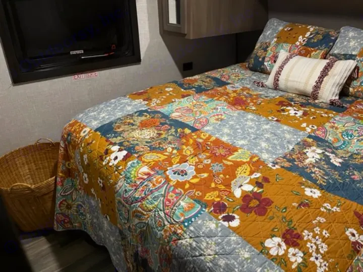 Inside a cozy RV rental bedroom: a vibrant patchwork quilt covers the bed, next to an emergency exit window.. Highland Ridge RV Open Range 2023