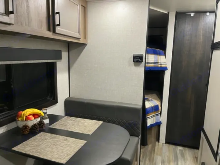 RV rental interior features a cozy dinette with bench seating, overhead cabinets, and built-in bunk beds.. Highland Ridge RV Open Range 2023