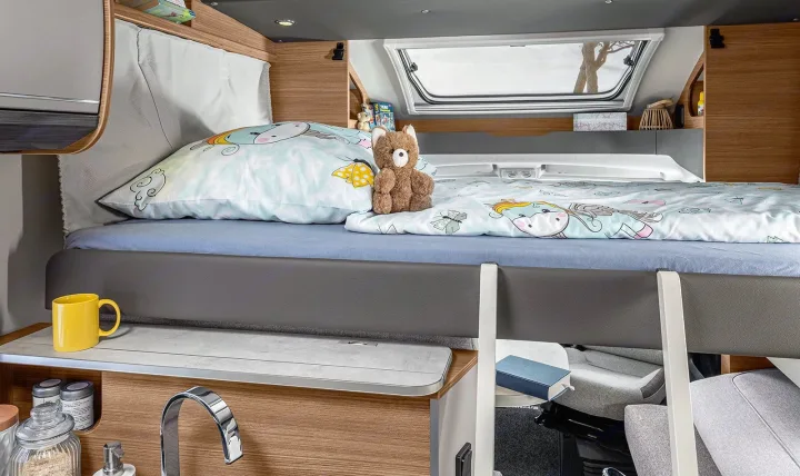 Cozy RV rental bunk bed for kids, featuring a cute unicorn bedding, teddy bear, and integrated sink area below.. Knaus live wave 2024