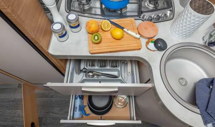Functional RV rental kitchen: overhead view of counter with stove, sink, fruit, and open drawers showing utensils & pots.. Knaus live wave 2024