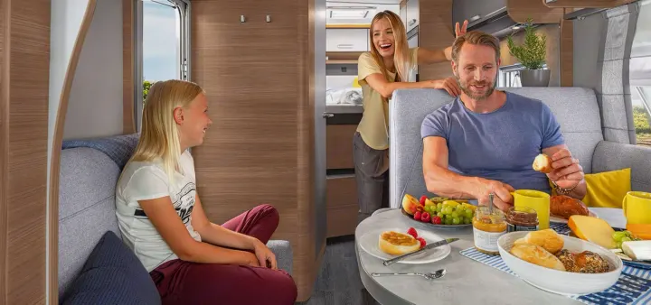 A family enjoys breakfast inside a spacious RV rental. This cozy camper offers comfort and fun for your travels.. Knaus live wave 2024