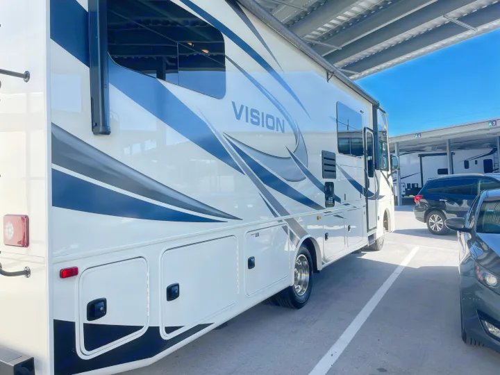Large white "VISION" RV rental with bold stripes, parked under cover. Ideal motorhome for travel adventures.. Entegra Coach Vision 2021