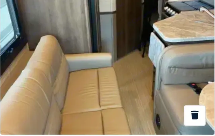 View inside an RV rental showing a light-colored sofa, wood-look flooring, and a compact kitchen/dinette area.. Entegra Coach Vision 2021