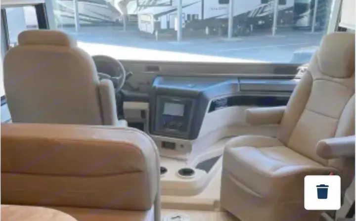 Spacious RV rental cockpit with tan captain's chairs and dashboard, offering a view of other RVs through the windshield.. Entegra Coach Vision 2021
