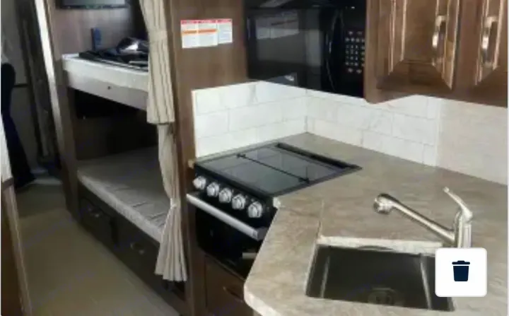 Modern RV rental interior with a well-equipped kitchen (stove, microwave, sink) and practical bunk beds.. Entegra Coach Vision 2021