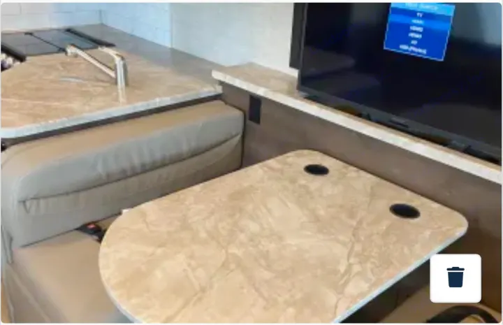 Inside an RV rental: a cozy dinette with a built-in table and TV, next to a functional kitchen area.. Entegra Coach Vision 2021