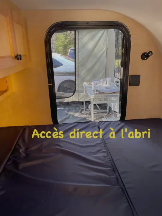 Cozy RV rental interior: comfortable bed & direct access to an outdoor dining shelter with table.. Car-gotrailers liberty2goXL 2021