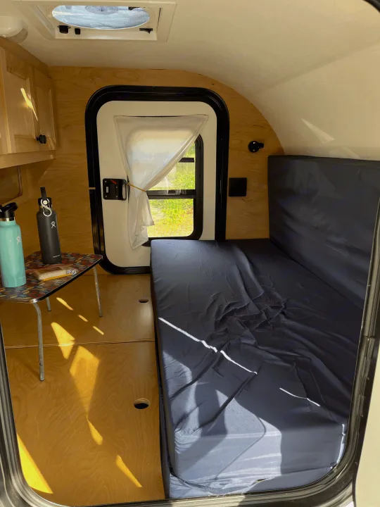 Inside a compact rv rental: bright interior, comfy bed, and wood details, ready for your next road trip.. Car-gotrailers liberty2goXL 2021