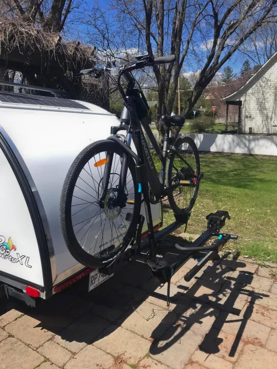 A bike mounted on a rack attached to a white RV rental, featuring solar panels on its roof for sustainable travel.. Car-gotrailers liberty2goXL 2021