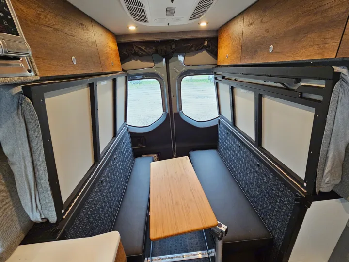 Inside this RV rental: a flexible camper van dinette/bed setup with benches, a table, wood cabinets, and rear windows.. Storyteller Overland Stealth Mode 2021