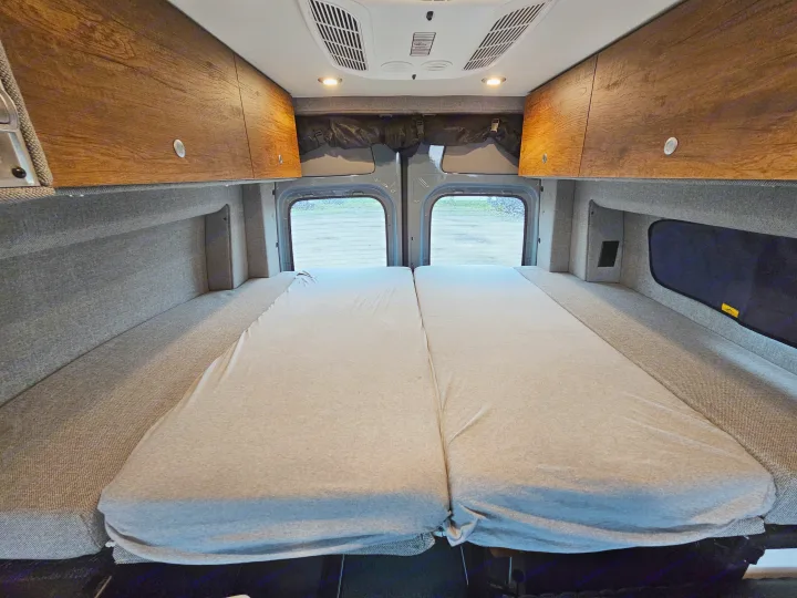 Experience comfort in this RV rental's cozy van interior. Features a plush bed, overhead storage, and rear windows.. Storyteller Overland Stealth Mode 2021