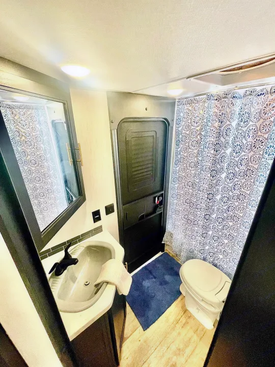 Compact RV rental bathroom featuring a sink, mirror, toilet, and patterned shower. Ideal for road trip comfort.. Forest River Cherokee Grey Wolf 2022